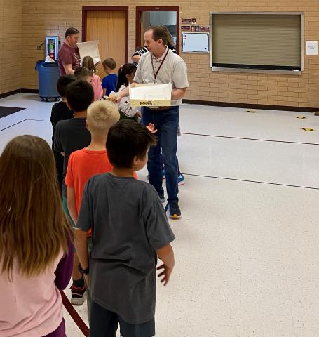 Mr. Gull and Mr. Cook handing out donuts to 3rd grade students. 