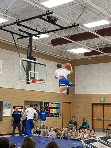 Another BYU dunk team member flying through the air to dunk the basketball while Rees students and teachers watch