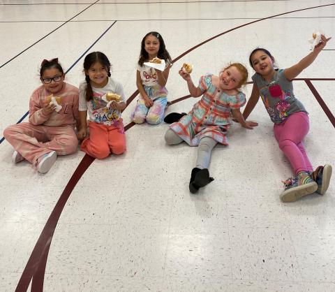 Five girls eating donuts in the gym together 