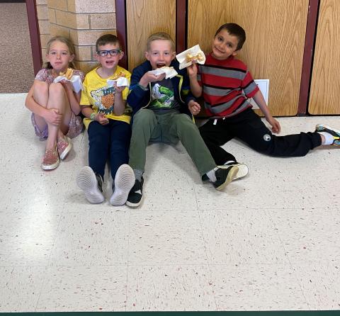 Four first grade students sitting down eating donuts