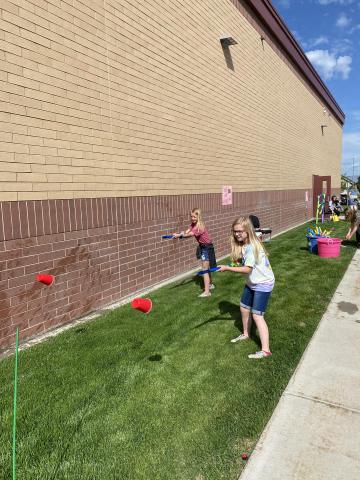 Rees students shooting water into cups at squirting game outside at the reading carnival. 