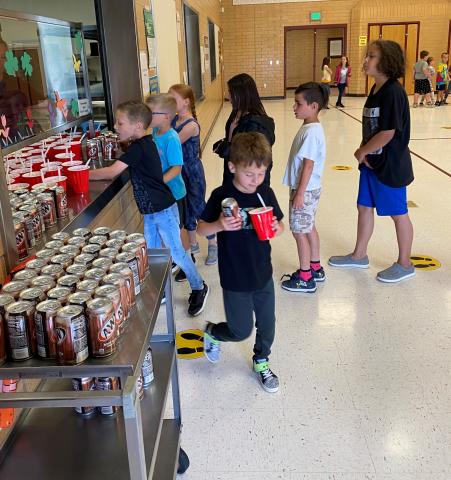 Boy smiling as he walks outside with his root beer float.  Other students in the back are lined up waiting for their treat