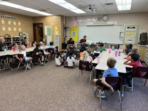 Football players reading a book to second grade students 
