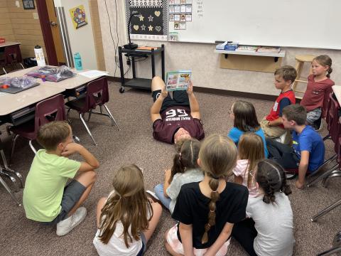 MMHS football player reading to a group of students as he lays on the floor