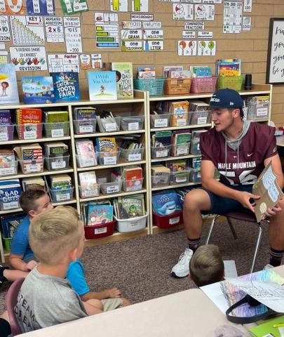 Football player reading to some Rees Students. 