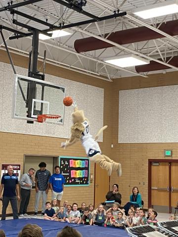 Cosmo flying through the air to dunk the basketball while Rees students and teachers watch