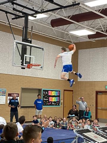 BYU dunk team member flying through the air to dunk the basketball while Rees students and teachers watch 