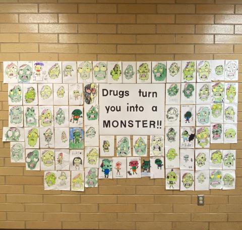 Wall with pictures of monsters drawn by second grade students and a saying "Drugs turn you into a MONSTER!"