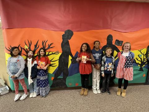 Rees 4th Grade students with their book club book standing in front of the characters they made from the book