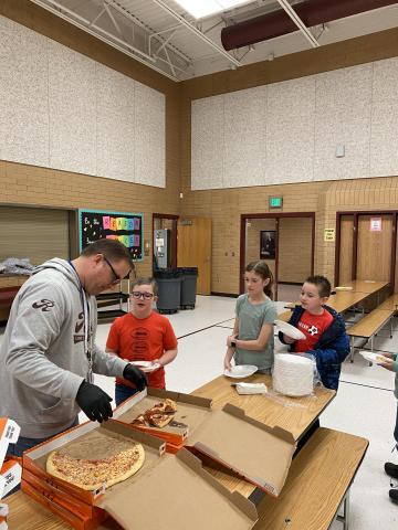 Mr. Gull serving pizza to three students. 