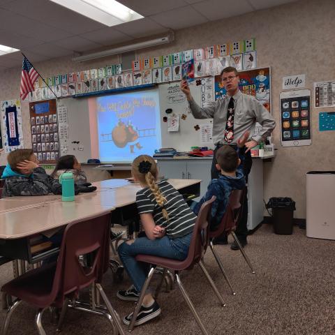 Mr. Nielsen holding up a Christmas book to read to Rees 5th grade students. 