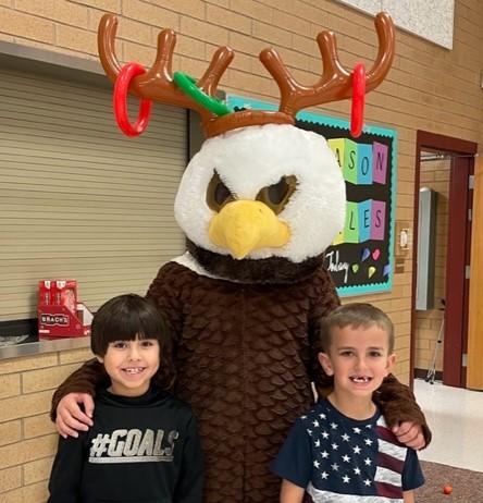 Rees eagles mascot wearing reindeer antlers standing with two second grade boys. 