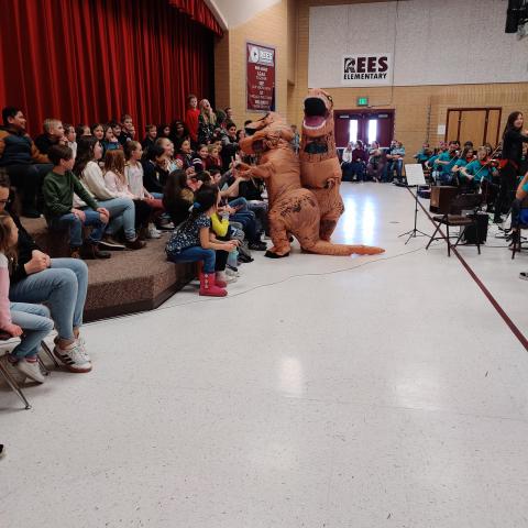Two blow-up T-Rex dinosaurs having fun with the Rees 5th grade students at the orchestra performance.