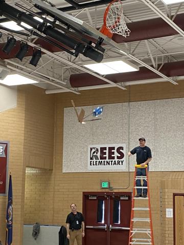 Mr. Jimmy on a ladder and Mr Cook helping during the egg drop. blue and brown cardboard  connected to an egg. 
