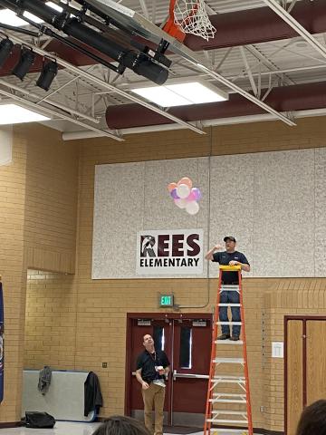 Mr. Jimmy on a ladder and Mr Cook helping during the egg drop. Pink balloons connected to an egg. 